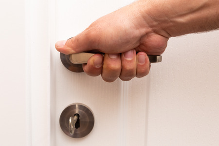 Hand touching metallic doorhandle of white wooden entranceの写真素材