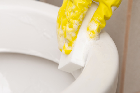 Close-up of white sponge with foam held by person wearing yellow gloves as cleaning conceptの写真素材