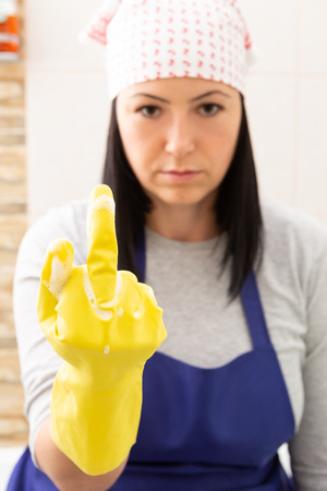 Angry woman wearing cleaning attire with blue apron and kerchief showing middle finger gesture as hate chores conceptの写真素材