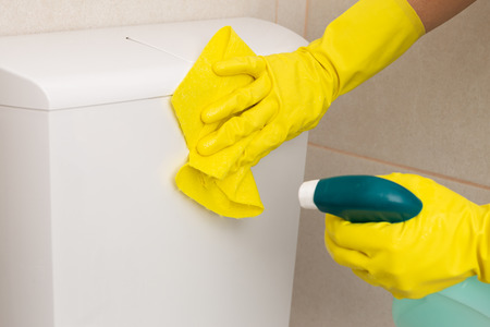 Person wearing gloves cleaning toilet with yellow cloth and spray as bathroom cleaning conceptの写真素材