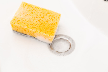 Yellow sponge with white foam inside sink close-upの写真素材