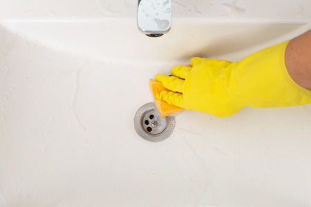 Person cleaning porcelain bathroom wink with foam using sponge and wearing yellow glovesの写真素材