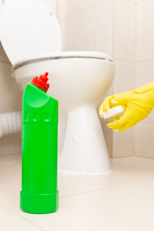 Green disinfectant bottle and white sponge held with yellow sanitary gloves in front of wc as chores conceptの写真素材