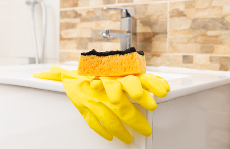 Yellow sanitary rubber gloves and orange sponge on edge of white porcelain sinkの写真素材