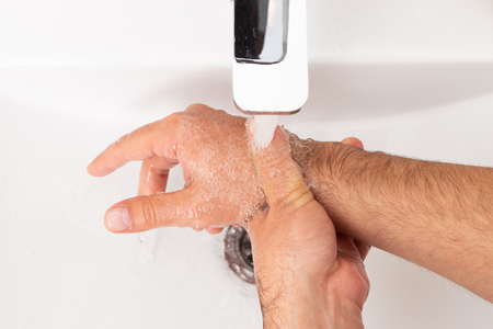 Man rinsing soapy hands under inox water tap runningの写真素材