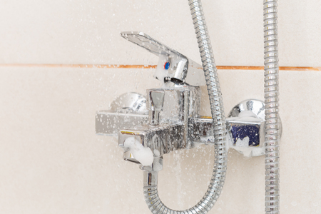 Water from shower running for rinsing metallic tap with foam close-upの写真素材