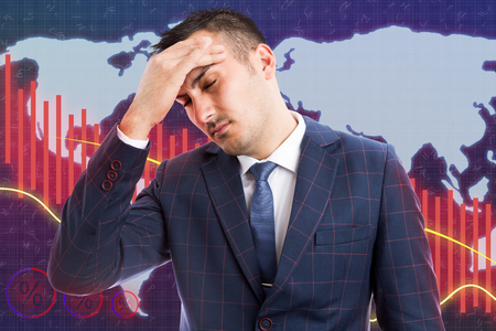 Male broker with headache caused by stress as economic decline concept on world map and red graph backgroundの写真素材
