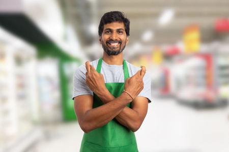 Friendly supermarket or hypermarket indian employee making good luck gesture with crossed fingers and arms in store backgroundの写真素材