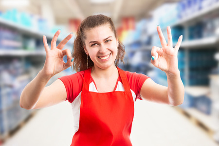 Female employee at hypermarket or supermarket making okay gesture with fingers at both hands and friendly expressionの写真素材