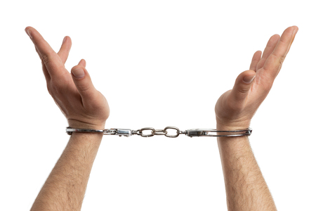 Closeup of handcuffed male hands rised as arrest concept isolated on white studio backgroundの写真素材