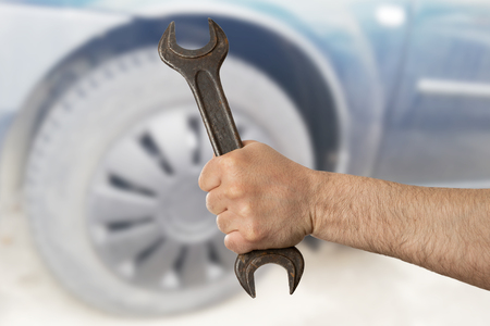 Male mechanic holding steel wrench focused closeup with car tire in backgroundの写真素材