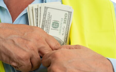Closeup of old male architect putting dollars in chest pocket of blue shirt isolated on white studio backgroundの写真素材