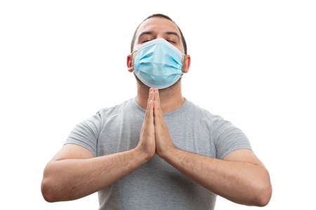 Faithful adult man making praying gesture using hands with eyes closed wearing covid19 pandemic protection disposable mask isolated on white backgroundの写真素材