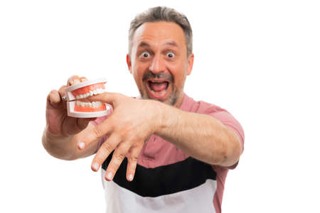 Close-up of shocked adult man having hand thumb finger bitten by fake teeth denture wearing casual...