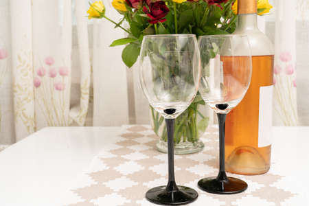 Two glasses and bottle of wine on table with roses flowers in vase as romantic date or celebrating...