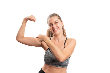 Cheerful woman model pointing index finger at biceps muscle as healthy workout concept wearing...