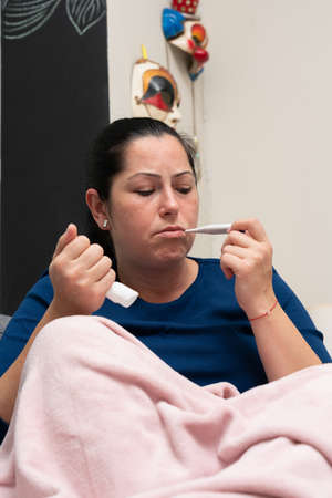 Sick female adult model measuring body temperature body temperature using thermometer as covid19 flu...