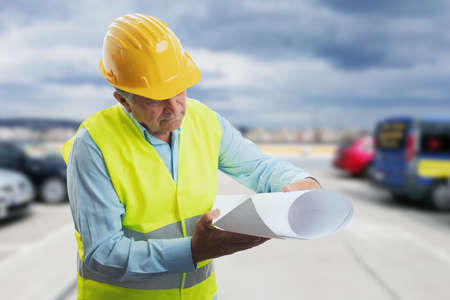 Focused old male architect contractor engineer in vest and yellow protective helmet equipment...