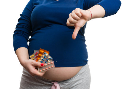 Close-up of pregnant woman holding medicines and making unlike gesture with hand as not good concept isolated on white backgroundの写真素材