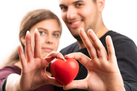 Close-up with selective focus of red heart held presented by cute girlfriend and boyfriend couple as romantic love concept isolated on white studio backgroundの写真素材