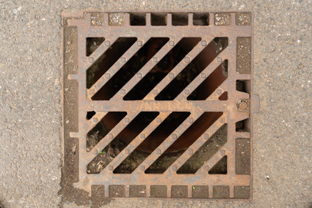 Close-up of sewer drain grate manhole made of steel metal on asphalt road as urban concept