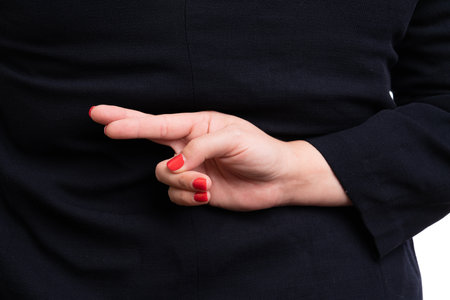 Close-up of adult businesswoman in formalwear making bad luck gesture with fingers crossed behind back as corporate concept isolated on white studio backgroundの写真素材