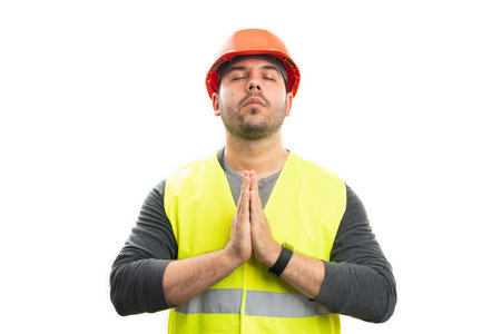Adult male builder holding hands together as prayer gesture faithful believer concept with eyes closed isolated on white studio backgroundの写真素材