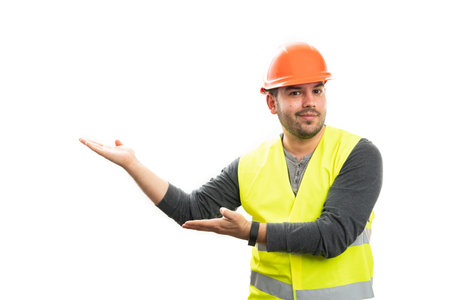 Adult friendly male builder in vest and safety helmet work attire smiling as presenting blank...