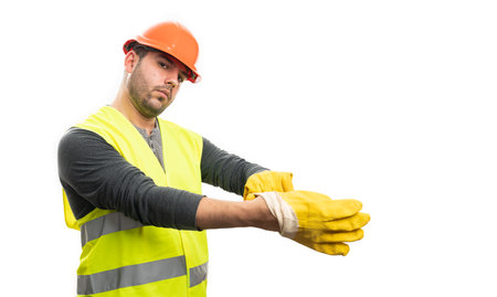 Serious constructor man getting ready for trades industry work wearing safety equipment orange hardhat and vest putting yellow gloves on isolated on white backgroundの写真素材