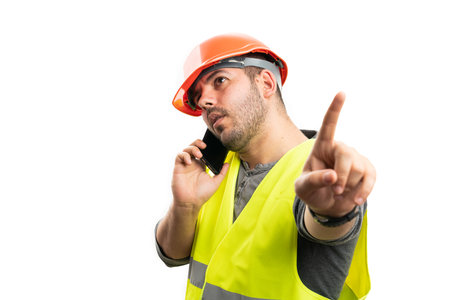 Male trades construction worker talking on phone with serious expression making wait gesture using...