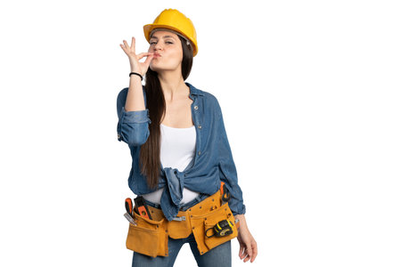 A confident female construction worker wearing a yellow hard hat and a tool belt makes a playful...