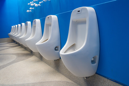 Row of white clean urinals on blue wall in public restroomの写真素材