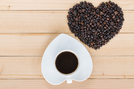 Heart shaped coffee cup and coffee beans on a wooden texture backgroundの写真素材