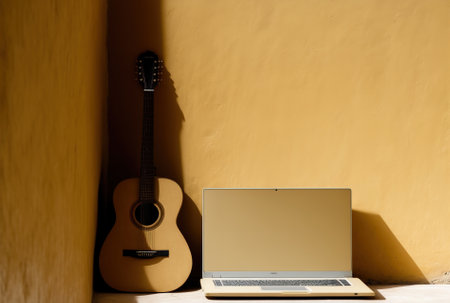 a laptop and an acoustic guitar against a tan backdrop upper level copy spaceの素材