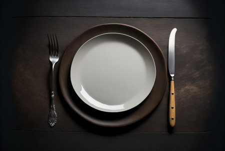 a top view a white circular plate a grey plate a napkin a wooden fork and a space on a dark tableの素材