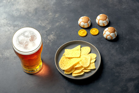 Beer and snacks copy space and a football on a gray table top. Football championship and playoff game munchiesの素材