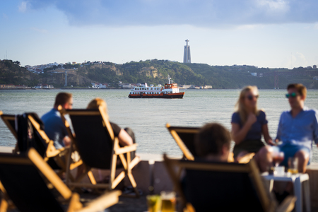 People in a esplanade in Lisbon, Portugal, by the Tagus River, with a passenger boat (cacilheiro) crossing the Tagus River; Concept for travel in Portugalのeditorial素材