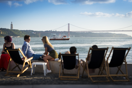 People in a esplanade in Lisbon, Portugal, by the Tagus River, with a passenger boat (cacilheiro) crossing the Tagus River; Concept for travel in Portugalのeditorial素材