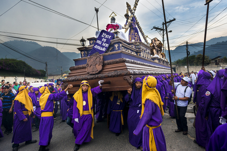 Antigua, Guatemala - April 16, 2014: Man wearing purple robes, carrying a float (anda) during the...