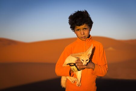 Merzouga, Morocco - April 12, 2016: Berber child holding a desert fox poses in the Erg Chebbi dunes in Morocco.のeditorial素材