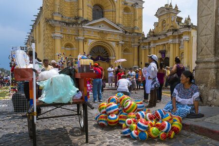 Antigua, Guatemala - April 17, 2014: Woman selling selling colorful rubber balls in a street of the old city of Antigua with the San Pedro Hospital on the background, in Guatemalaのeditorial素材