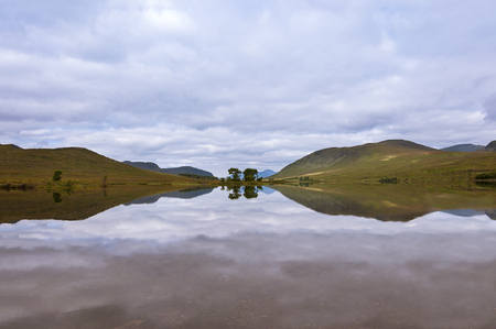 Beautiful lake with reflections of the trees and surrounding mountains in the Scottish Highlands, in Scotland, United Kingdom; Concept for travel in Scotlandの写真素材