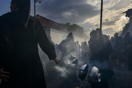 Antigua, Guatemala - April 19, 2014: Silhouette of men wearing black robes and hoods spreading...