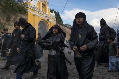 Antigua, Guatemala - April 19, 2014: Young boys wearing black robes and hoods spreading incense in a street of the city of Antigua during a procession of the Holy Week in Antigua, Guatemalaのeditorial素材