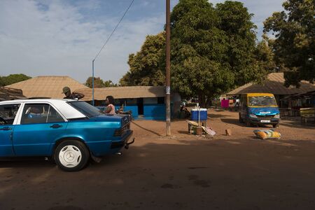 Bissau, Republic of Guinea-Bissau - January 28, 2018: View of a dirt road in a street of a slum in the city of Bissau with people entering in a taxi, in Guinea-Bissau, West Africaのeditorial素材
