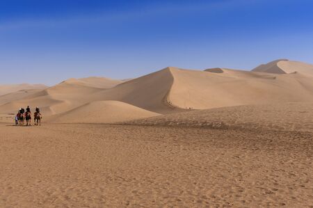 Dunhuang, China - August 8, 2012: Tourists riding cammels at the Echoing Sand Mountain near the city of Dunhuang, in the Gansu Province, China.のeditorial素材