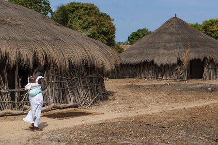 Orango Island, Guinea-Bissau - February 3, 2018: A mother carrying his small child on the back at the village of Eticoga in the island of Orango.のeditorial素材