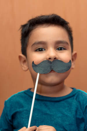 Little kid joking with a fake paper moustache.