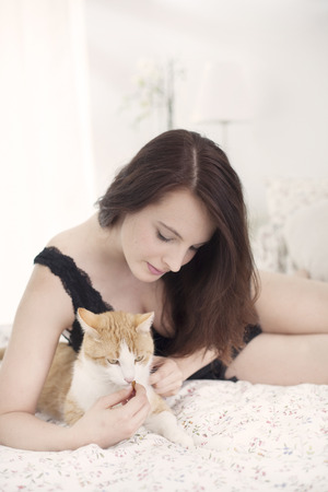 Beautiful young woman with cat in bedの写真素材