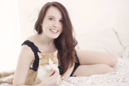 Beautiful young woman with cat in bedの写真素材